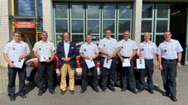 : Acht Männer in Feuerwehrkleidung stehen auf dem Hof der Feuerwehr und präsentieren ihre Urkunden.