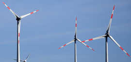 Rot-weiß gestreifte Rotorblätter von drei Windrädern vor einem blauen Himmel