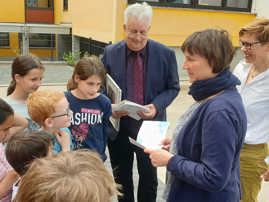 Baudezernent Andreas Ludwig, Beate Brucksch und Zeichnerin Teresa Habild verteilen die Malhefte an die Grundschulkinder
